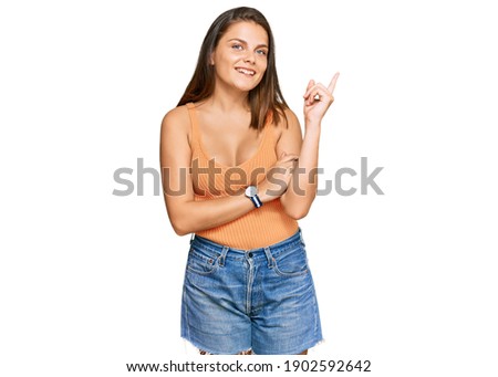 Young caucasian woman wearing casual clothes with a big smile on face, pointing with hand and finger to the side looking at the camera. 