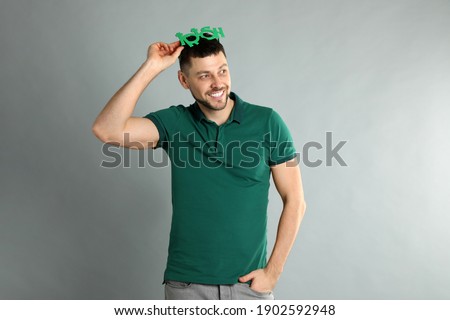 Happy man in green shirt and party glasses on light grey background. St Patrick's Day celebration