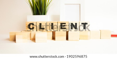 Wooden cubes with letters on a white table. The word is CLIENT. White background with photo frame, house plant.