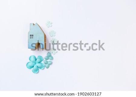 Wooden blue house model with blue paper flower on white background, invitation card background idea, new house