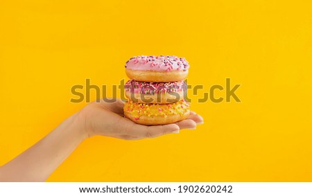round pink and yellow very appetizing glazed doughnuts with sprinkles on palm of light-skinned person on bright yellow background. Order and deliver food online, food blog content, selective focus