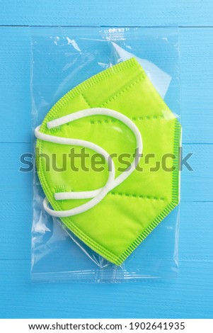 Green fashionable medical mask KN95 with white rubber bands for ears in plastic packaging on a blue board. Medical supplies delivery concept
