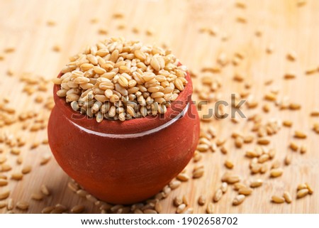 Wheat grains in clay pot on white background