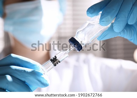 Woman filling syringe with vaccine from vial on blurred background, closeup Royalty-Free Stock Photo #1902672766