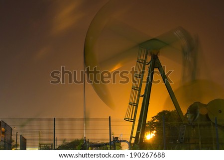 Night viewof an oil pump illuminated by flares of an refinery plant