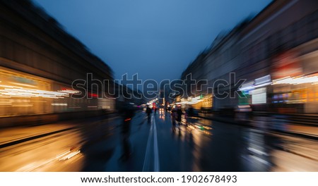 on the street in the evening bright blurry lights from shops traffic lights car headlights wet road in the city among blurred home perspective home dividing white stripe in the middle of the street