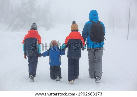Family, father with three children and dog, walking in deep snow and fog in the mountains