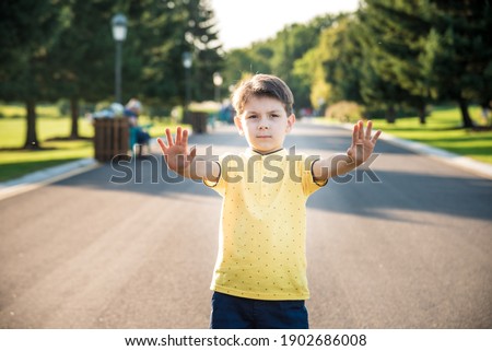 Happy child making a stop sign with his hand while standing at the road.