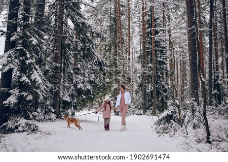 Happy family young mother and little cute girl in pink warm outwear walking having fun with red shiba inu dog in snowy white cold winter forest outdoors. Family sport vacation activities