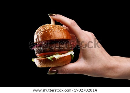 female hand holding mini burger as a Christmas tree toy on black background