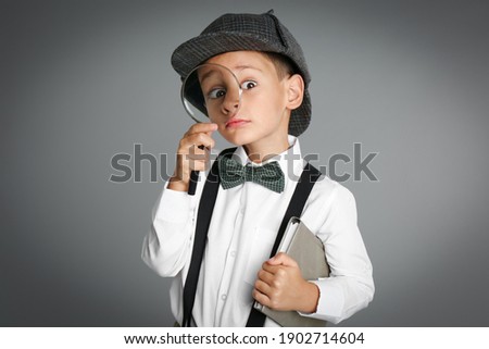 Little boy with magnifying glass playing detective on grey background