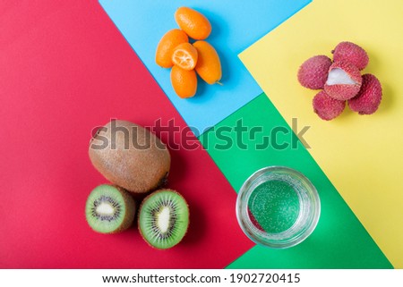 Lychee, kiwi, kumquat and a glass of water on geometric multicolored background. Assorted tropical fruits. Trendy flat lay