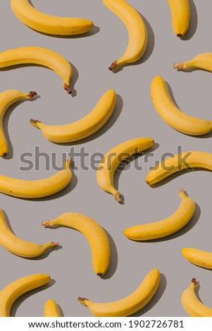 Creative pattern made with illuminating yellow bananas on a gray background. Minimal summer aesthetic concept.