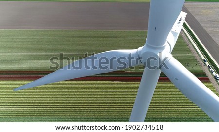 Aerial close up view of windturbine and polder landscape tulip field in background these turbines are used to provide renewable power by using kinetic energy of the wind Royalty-Free Stock Photo #1902734518