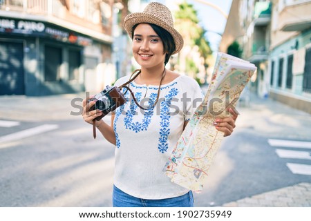 Young latin tourist girl on vacation holding map and vintage camera at the city.