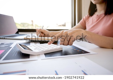 Businesswoman bookkeeper hand use calculator and analysis the graph with laptop at the home office for setting challenging business goals And planning to achieve the new target.