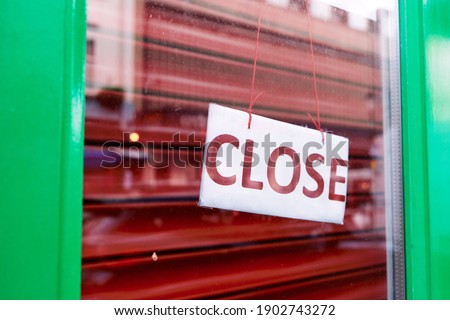 Paper sign saying Close hanging behind glass of green door with red shutters inside