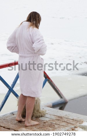 Winter swimming sport, a mature Caucasian woman in a white bathrobe getting ready for a swim in the ice hole water at frosty winter day, healthy lifestyle.