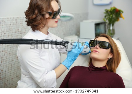 beautician removes facial hair of a woman wearing goggles. face laser hair removal procedure