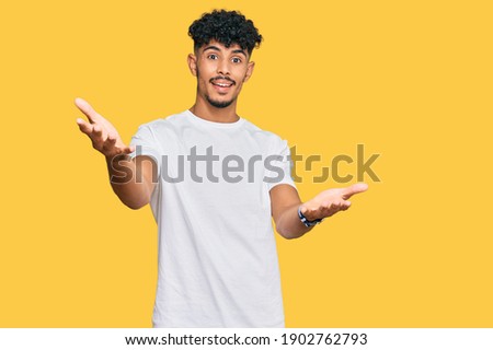Young arab man wearing casual white t shirt smiling cheerful offering hands giving assistance and acceptance. 
