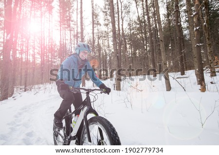 An attractive woman rides her fat bike on a trail in the snow.