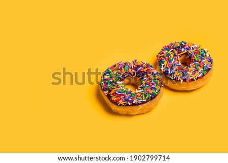 Two of chocolate frosted donuts with sprinkles on yellow background. Playful and joyful tasty sugary comfort food for customers with copy space.