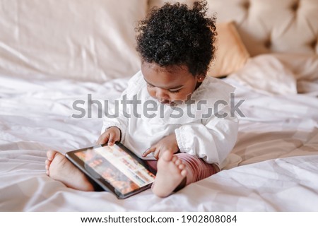 Mixed race African black toddler baby girl watching cartoons on tablet. Ethnic diversity. Little kid child using technology. Early age education development. Video chat, video call.