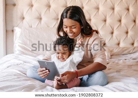 Mixed race Indian black mother with toddler baby girl watching cartoons on tablet. Ethnic diversity. Family mom with kid using technology. Video chat, video call. Black people community.