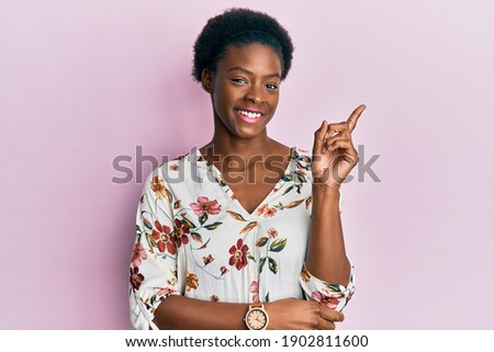 Young african american girl wearing casual clothes with a big smile on face, pointing with hand and finger to the side looking at the camera. 