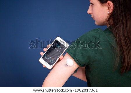 Girl checking glucose level with a remote sensor and mobile phone. Continuous glucose monitor. Royalty-Free Stock Photo #1902819361