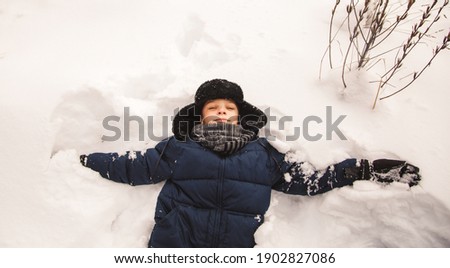 The boy is lying in the snow. Winter on the street makes a snow angel