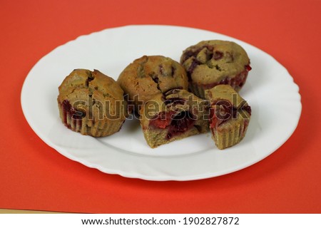 three whole muffins made of rice flour, yogurt, cherries and pumpkin oil and one cut in half lie on a white plate on a red background side view . gluten-free homemade cakes