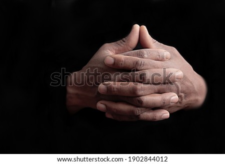 man praying to god with hands together on black background stock photo