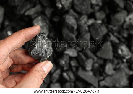 Man holding piece of coal over pile, closeup. Space for text Royalty-Free Stock Photo #1902847873