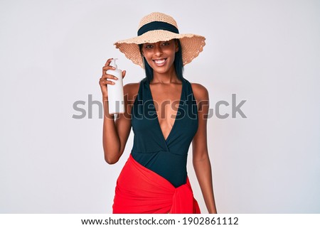 Young african american woman wearing swimsuit and holding sunscreen lotion looking positive and happy standing and smiling with a confident smile showing teeth 