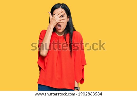 Beautiful young woman wearing casual clothes peeking in shock covering face and eyes with hand, looking through fingers with embarrassed expression. 