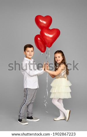 Happy couple of little girl and boy with red heart balloons isolated on gray background. St. Valentine's Day