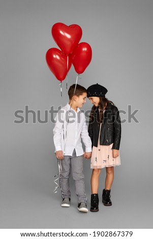fashionable couple of little girl and boy with red heart balloons isolated on gray background. St. Valentine's Day