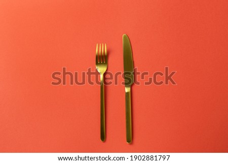 Fashionable golden mat cutlery, fork, knife on red paper, minimal style flat lay, copy space. For restaurant, cafe, delivery service, social media. Concept Valentine's day food. Horizontal.