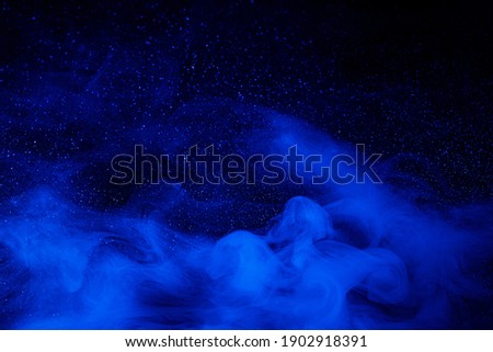 Abstract blue smoke moves on black background. Beautiful swirling smoke rolling low across the ground.