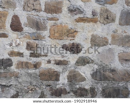 A wall with masonry of various shapes of stone and a thick gray layer of cement between them. Texture not seamless. Closeup photo