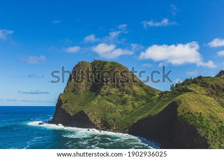 Kahakuloa Head juts out into the ocean. Green volcanic island peak against blue sky 