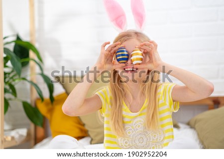 Happy Easter kids. Girl in rabbit bunny ears on head with colored eggs at home. Cheerful crazy smiling child