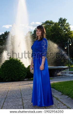 Pretty teen girl with makeup smiling and posing in the park. Female model with elegant hairstyle. Fountain in background