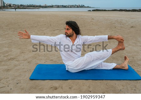 Stock photo of adult man with long hair doing yoga poses in the beach.