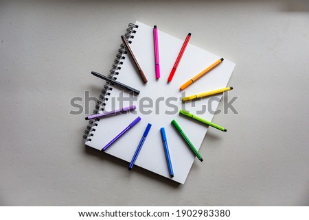 Flat lay of a notebook with colorful art supplies over a clear background