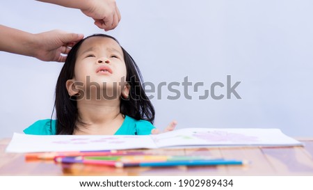 Mom's hand was attached hairpin to the front hair for her daughter who is about to study art. Child look up at adults to make it easier to attach hairpin. Children 3-4 years old. White wall background