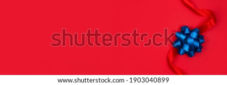 Festive banner with decorative blue ribbon bow on red background with copy space for text. Giving presents concept. Festive composition for greeting card or holidays sale background, selective focus