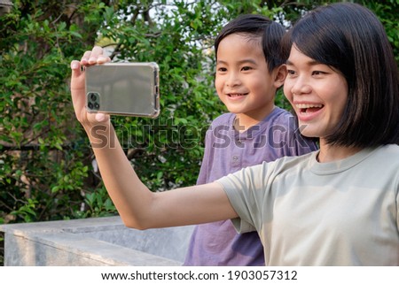 An Asian mother and child taking a selfie with a smiling face at home.
