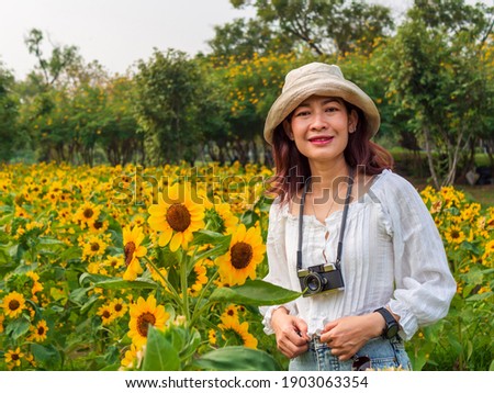 Portrait of 30-40s Asian women wearing white hats, wearing white shirts. Taking a picture with a toy camera In the park Full of green grass And sunflowers happily on a bright day With her holiday
